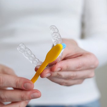 Woman using yellow toothbrush to clean clear aligner
