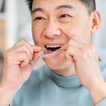 Man smiling while putting on clear aligner