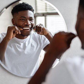 Man smiling at reflection while flossing in bathroom