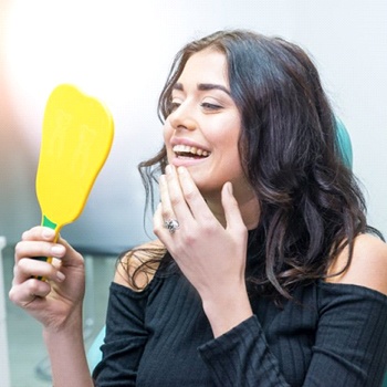 woman admiring her smile in a mirror in dental chair