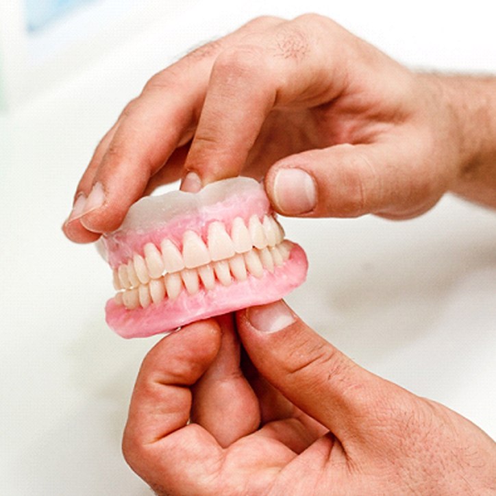 Person handling their dentures over a sink