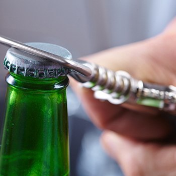 Close up of bottle opener opening green bottle