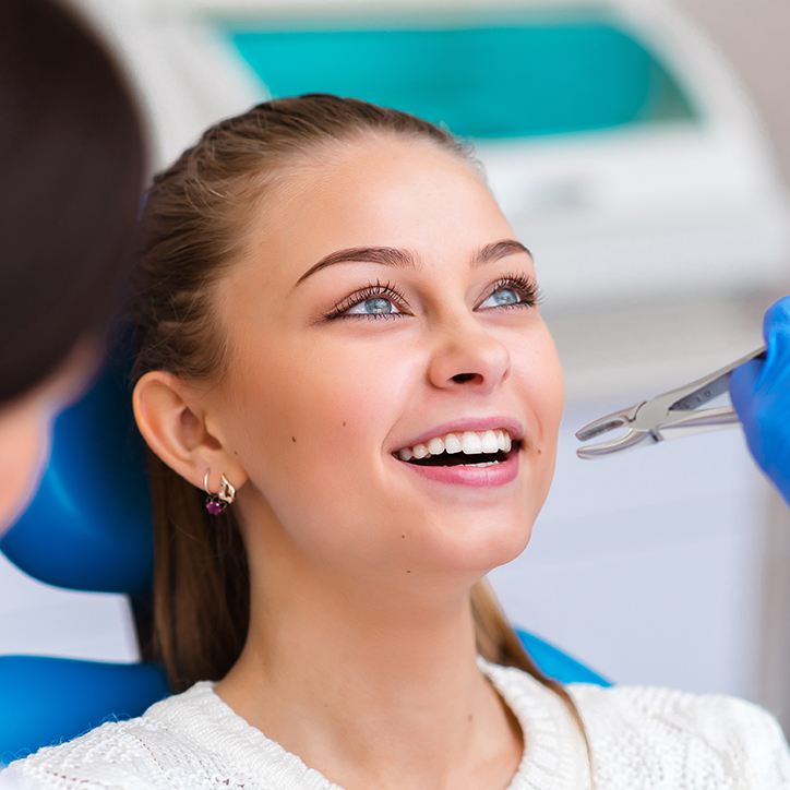 Dentist approaching woman’s teeth with forceps