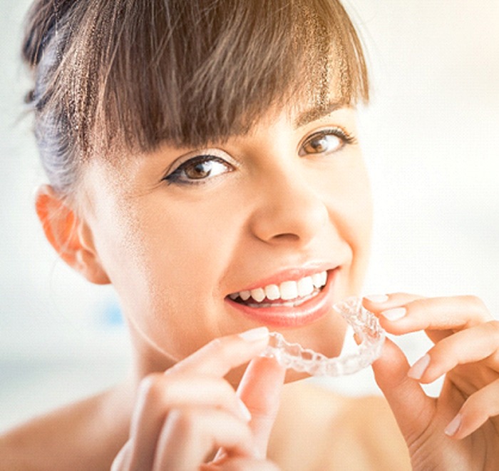 Woman smiling while putting Invisalign tray in