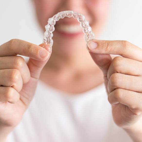 Smiling woman holding out Invisalign in Long Beach