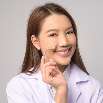 Woman smiling while holding up Invisalign aligner