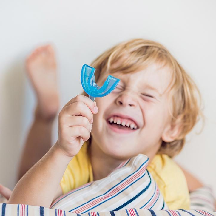 Child holding mouthguard during pediatric orthodontic treatment