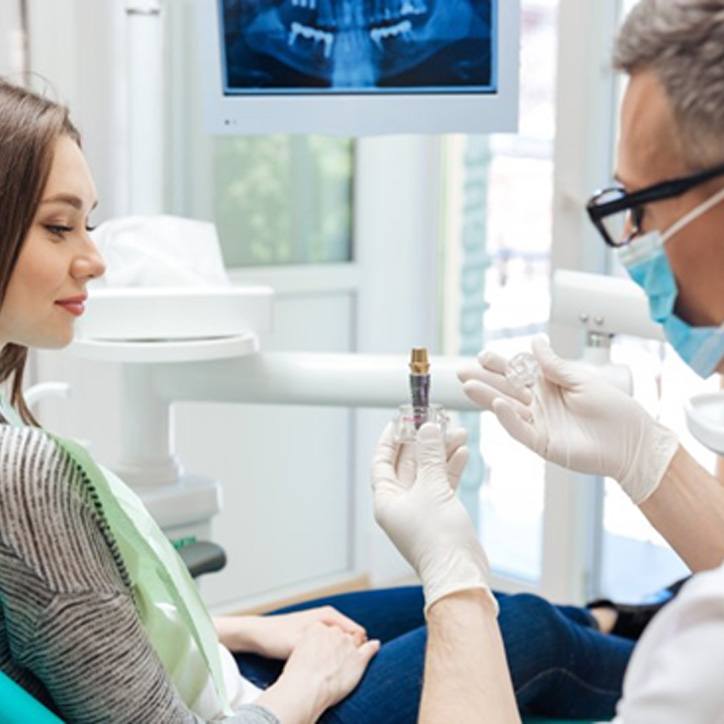 A dentist holding a dental implant in front of a patient