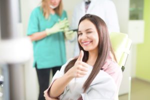 Teen girl with brown hair in yellow dentist chair smiling, winking, and giving a thumbs up
