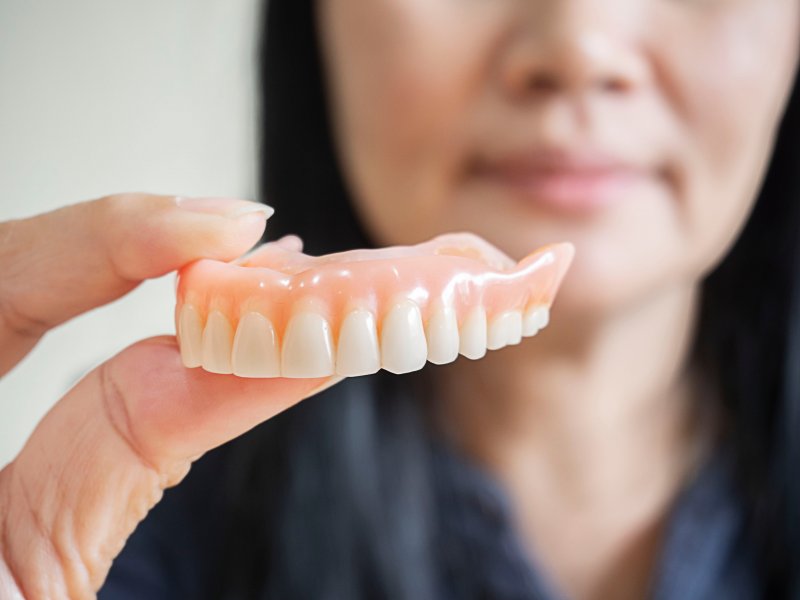 A woman holding a denture between her fingers