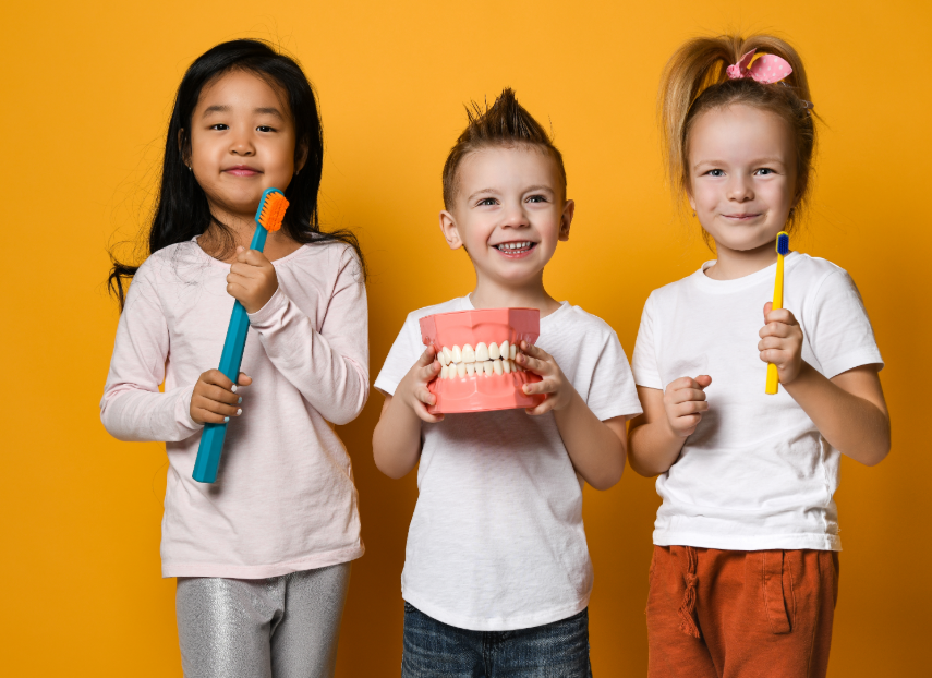 Kids smiling and holding toothbrushes and a model denture